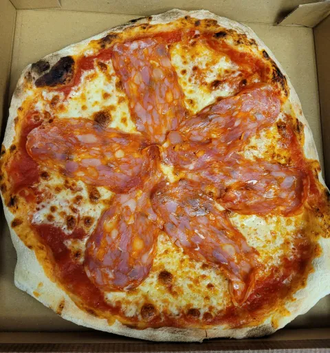 Pizza avec sa sauce tomate et ses tranches de spianata, une charcuterie légèrement épicée.